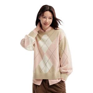 Woman wearing a pink and beige argyle sweater on a light background
