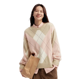 Woman wearing a pink and beige argyle sweater holding a brown paper bag on a white background