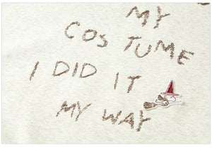 Text on sand with a broom and witch hat graphic, indicating a Halloween costume theme.