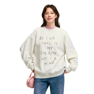 Person wearing a light-colored sweatshirt with text, standing against a plain background