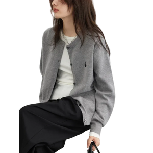 Person wearing a gray cardigan with a brand logo, sitting on a white chair against a light background.