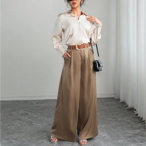 Woman wearing a beige blouse and wide-leg pants with a belt, standing against a plain background.