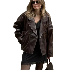 Woman wearing a brown leather jacket and sunglasses against a building wall.