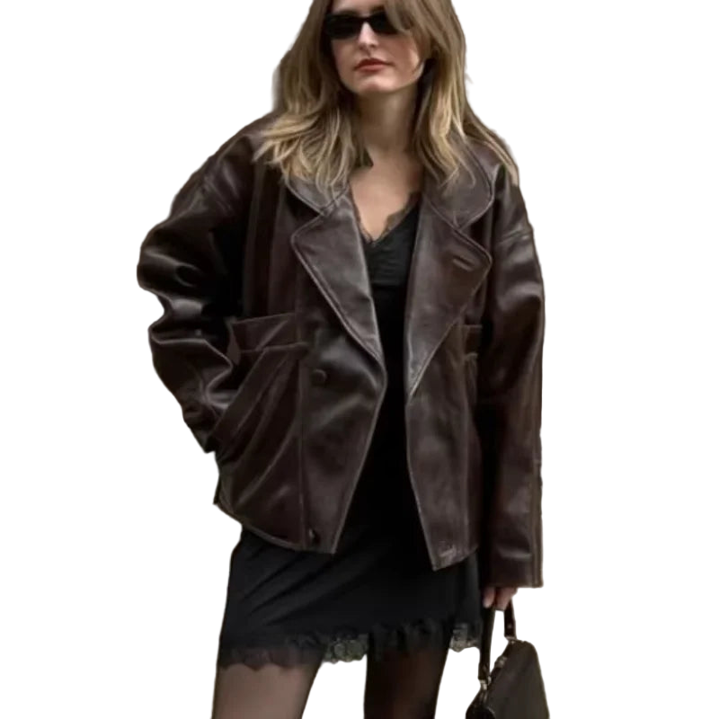 Woman wearing a brown leather jacket and sunglasses against a building wall.