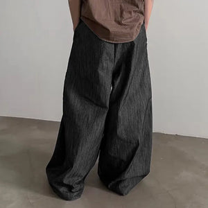 Person wearing wide-leg dark pants and a brown top against a plain background
