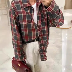 Person wearing a plaid shirt over a white top with a red handbag, standing against a light-colored floor.