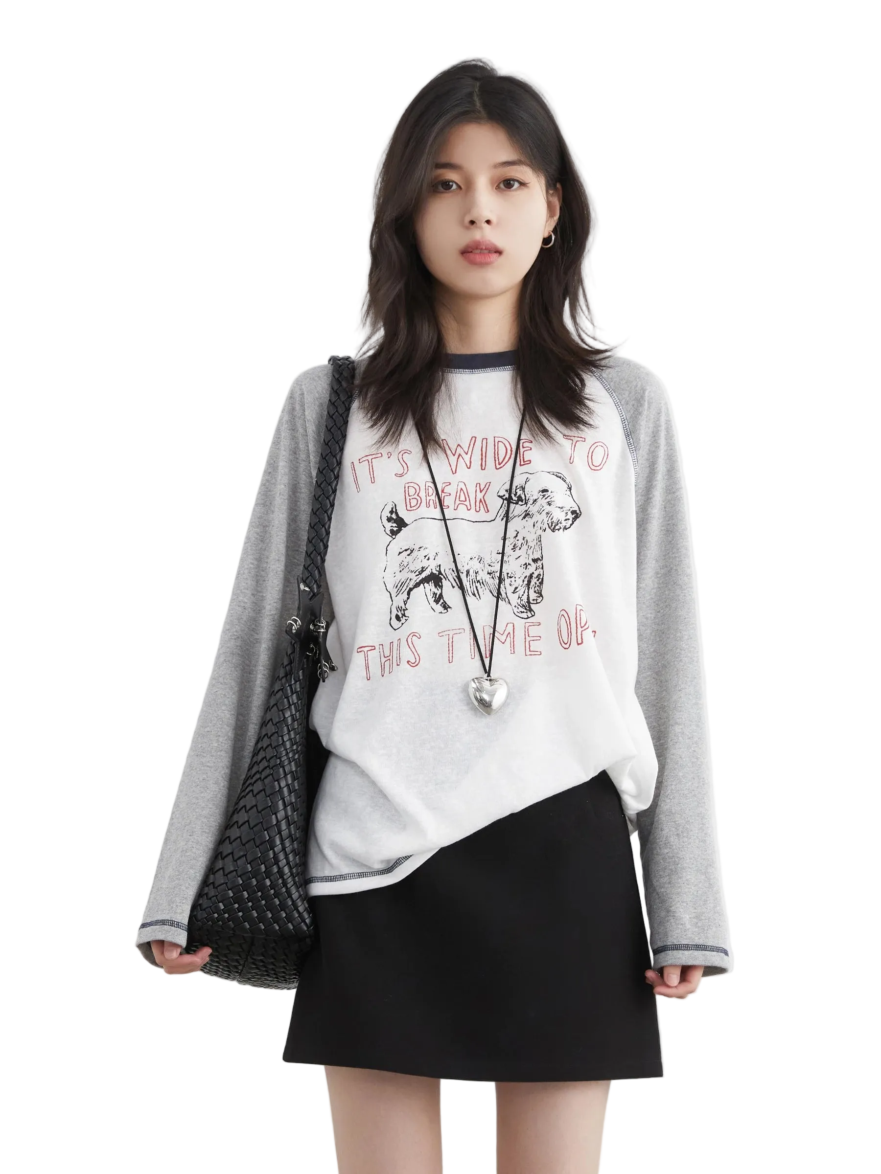 Woman wearing a gray sweater over a white graphic t-shirt and black skirt on a white background