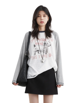 Woman wearing a gray sweater over a white graphic t-shirt and black skirt on a white background