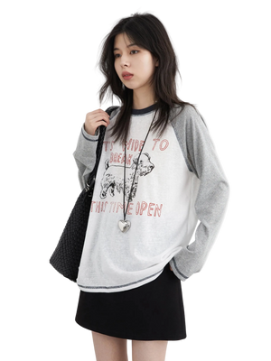 Woman wearing a gray oversized sweater with text and graphics, holding a black bag on a white background