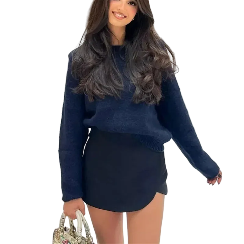 Woman wearing a blue sweater and black skirt holding a patterned handbag.