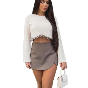 Woman wearing a white cropped sweater and gray skirt against a stone wall.