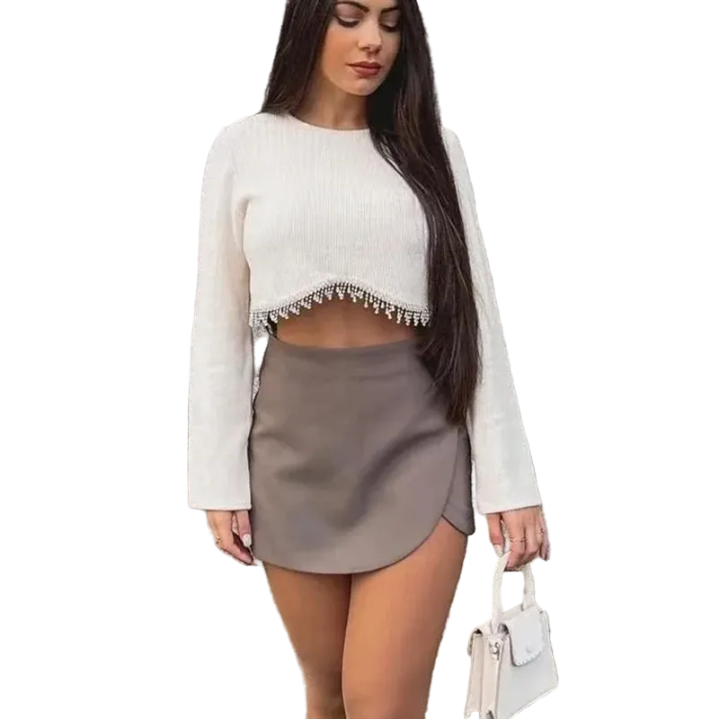 Woman wearing a white cropped sweater and gray skirt against a stone wall.
