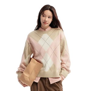 Woman wearing a pink and beige argyle sweater holding a brown paper bag on a light background
