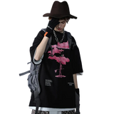 Person wearing a black outfit with a pink flamingo design, holding a phone, on a gray background