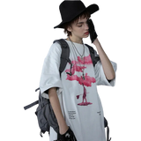 Person wearing a white t-shirt with a graphic design, black hat, and gray backpack against a plain background