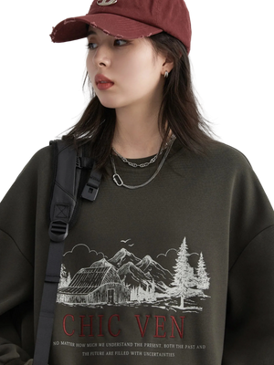 Person wearing a dark sweatshirt with a graphic design and text, standing against a plain background.