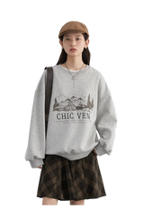 Person wearing a gray sweatshirt with a graphic design and text, standing against a plain background