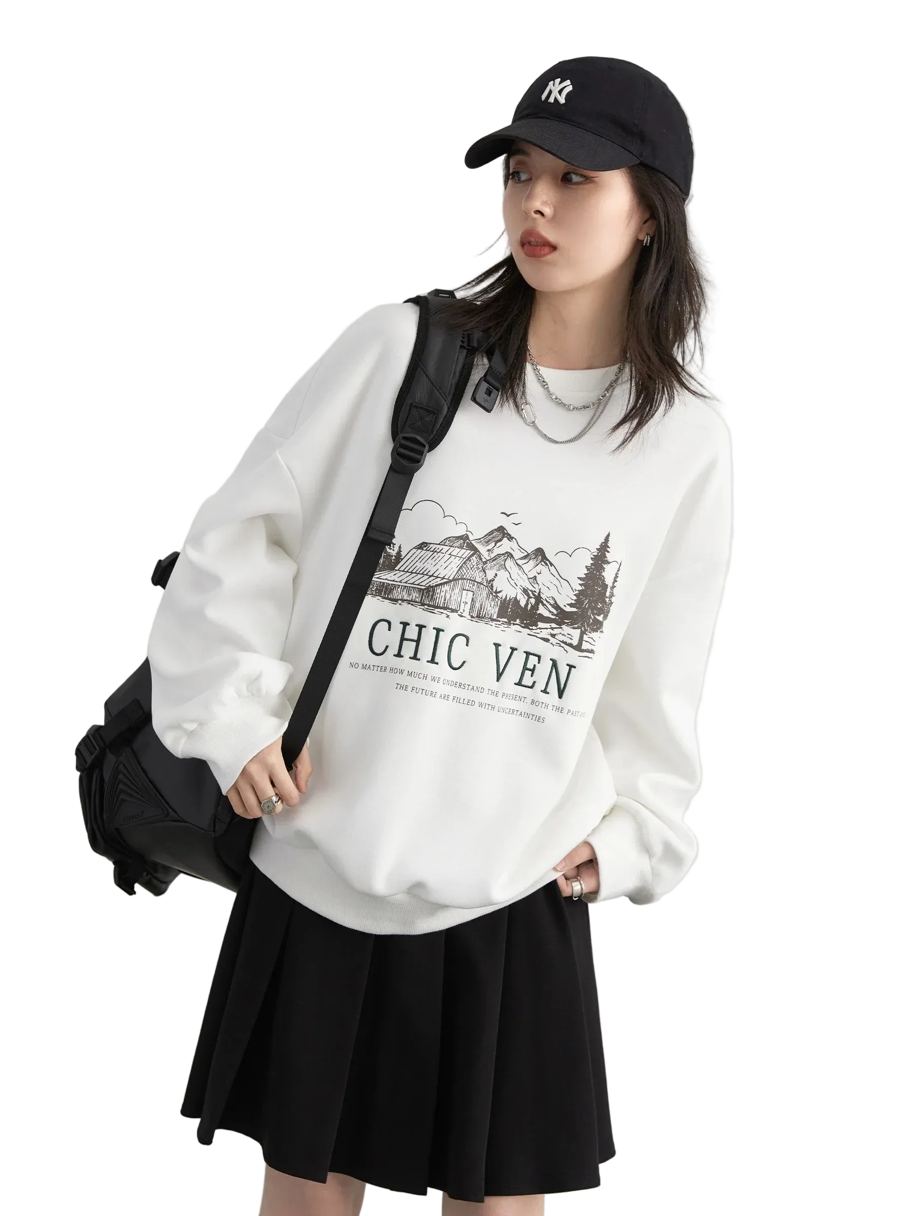 Person wearing a white sweatshirt with text and graphics, black skirt, and black cap on a light gray background