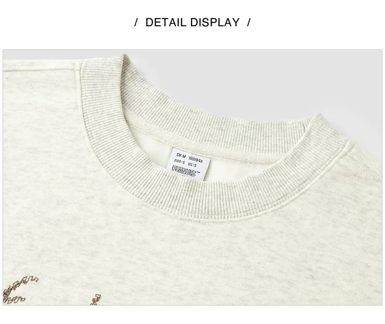 Close-up of a cream-colored sweater with a brand label on a light gray background