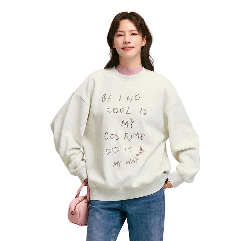 Person wearing a light-colored sweatshirt with text, standing against a plain background
