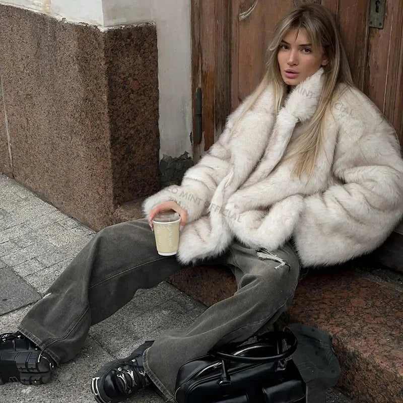 Person wearing a white fur coat sitting on a step holding a drink.
