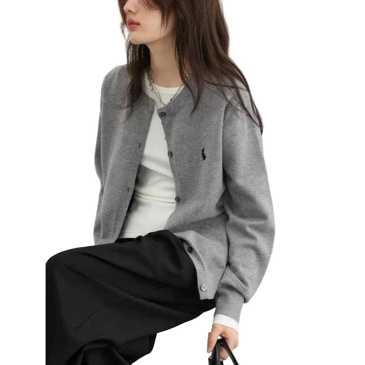 Person wearing a gray cardigan with a brand logo, sitting on a white chair against a light background.