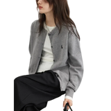 Person wearing a gray cardigan with a brand logo, sitting on a white chair against a light background.