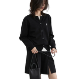 Person wearing a black cardigan with a brand logo, holding a black handbag on a white background