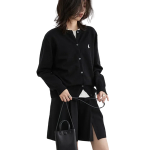 Person wearing a black cardigan with a brand logo, holding a black handbag on a white background