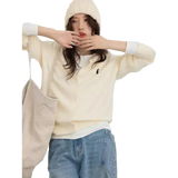 Person wearing a cream-colored sweater with a logo, light blue jeans, and a beige coat on a white background