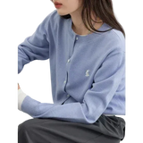 Person wearing a light blue sweater with a logo, sitting on a white chair.