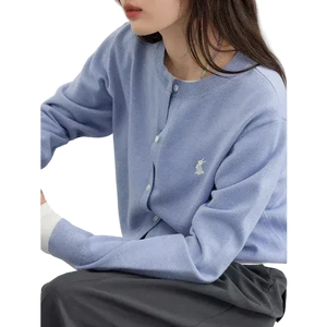 Person wearing a light blue sweater with a logo, sitting on a white chair.