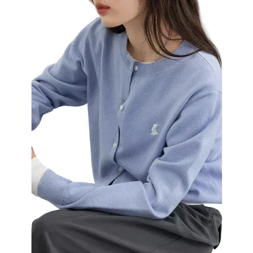 Person wearing a light blue sweater with a logo, sitting on a white chair.