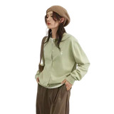 Person wearing a light green shirt and brown pants with a beige beanie on a white background