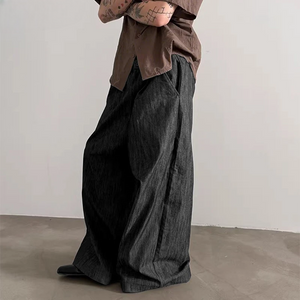 Person wearing a brown shirt and dark wide-leg pants against a plain background