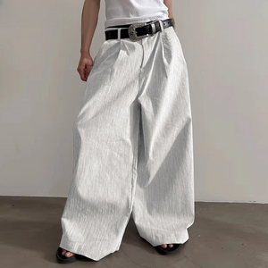 Person wearing wide-leg white pants with a black belt against a plain background