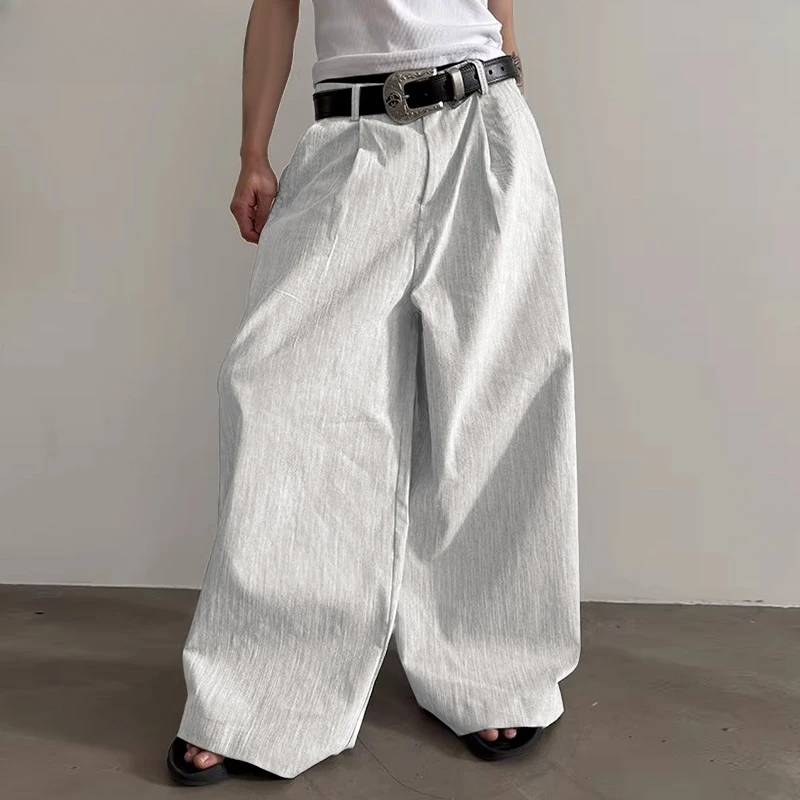 Person wearing wide-leg white pants with a black belt against a plain background