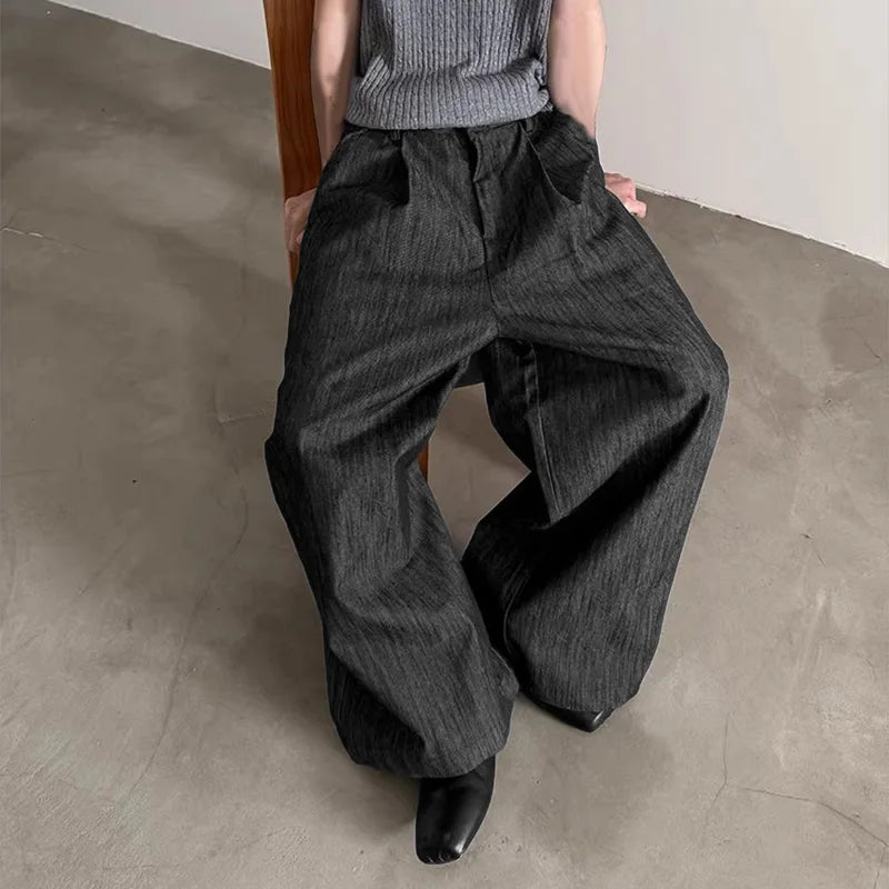 Person wearing gray wide-leg pants and a gray sweater sitting on a chair.