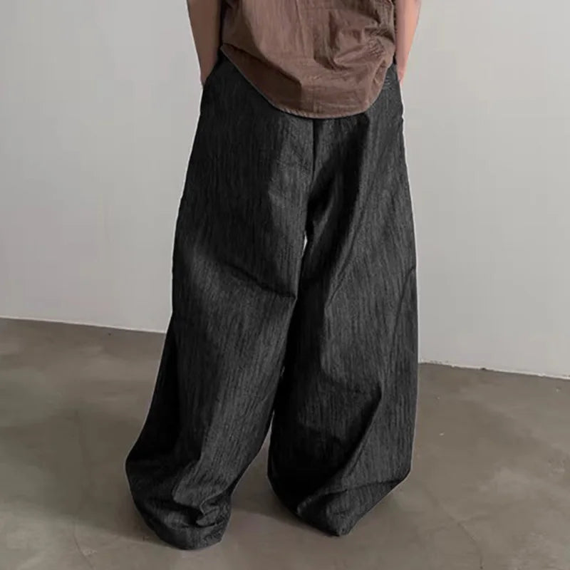 Person wearing wide-leg dark pants and a brown top against a plain background