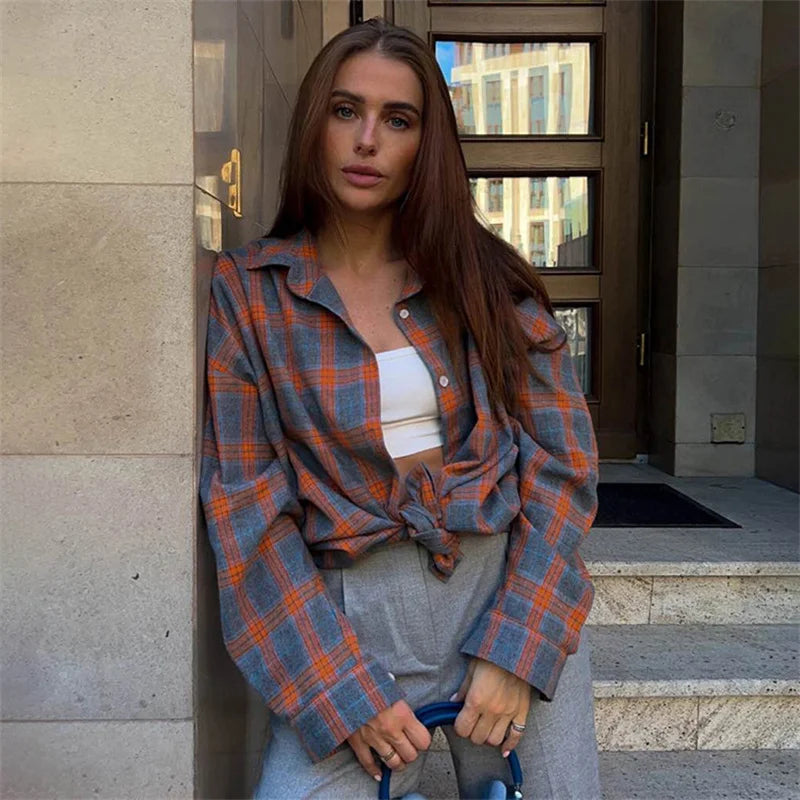 Woman wearing a plaid shirt leaning against a building entrance.