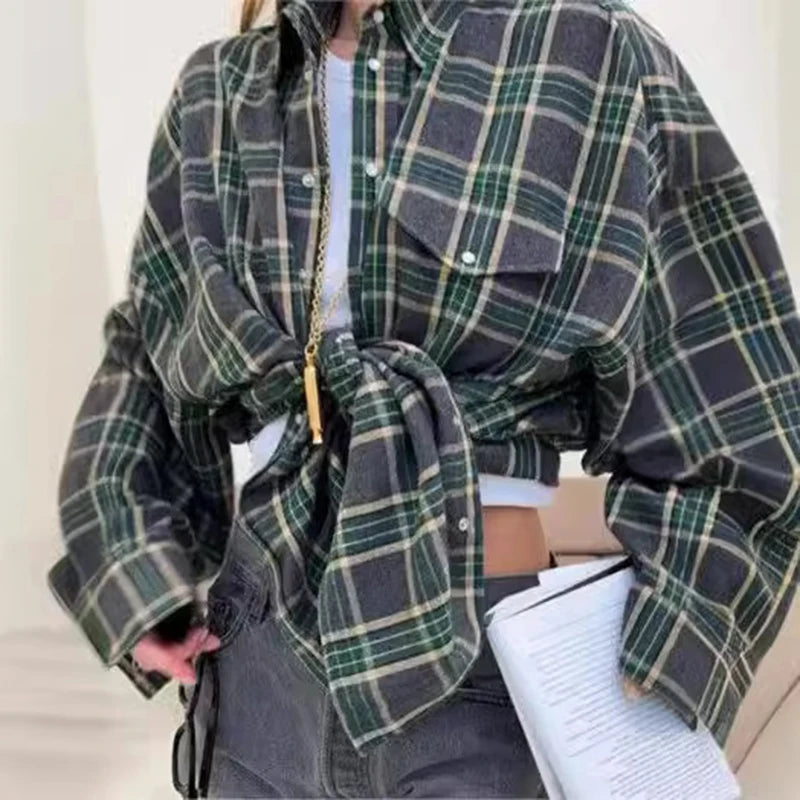 Person wearing a green and gray plaid shirt with a belt, holding a notebook.