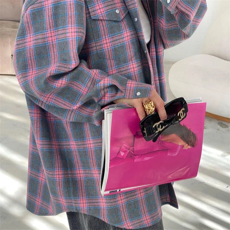 Person wearing a plaid coat holding a pink magazine with a blurred background