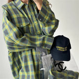 Person wearing a green and yellow plaid shirt with a black cap and Chanel bag in the foreground.