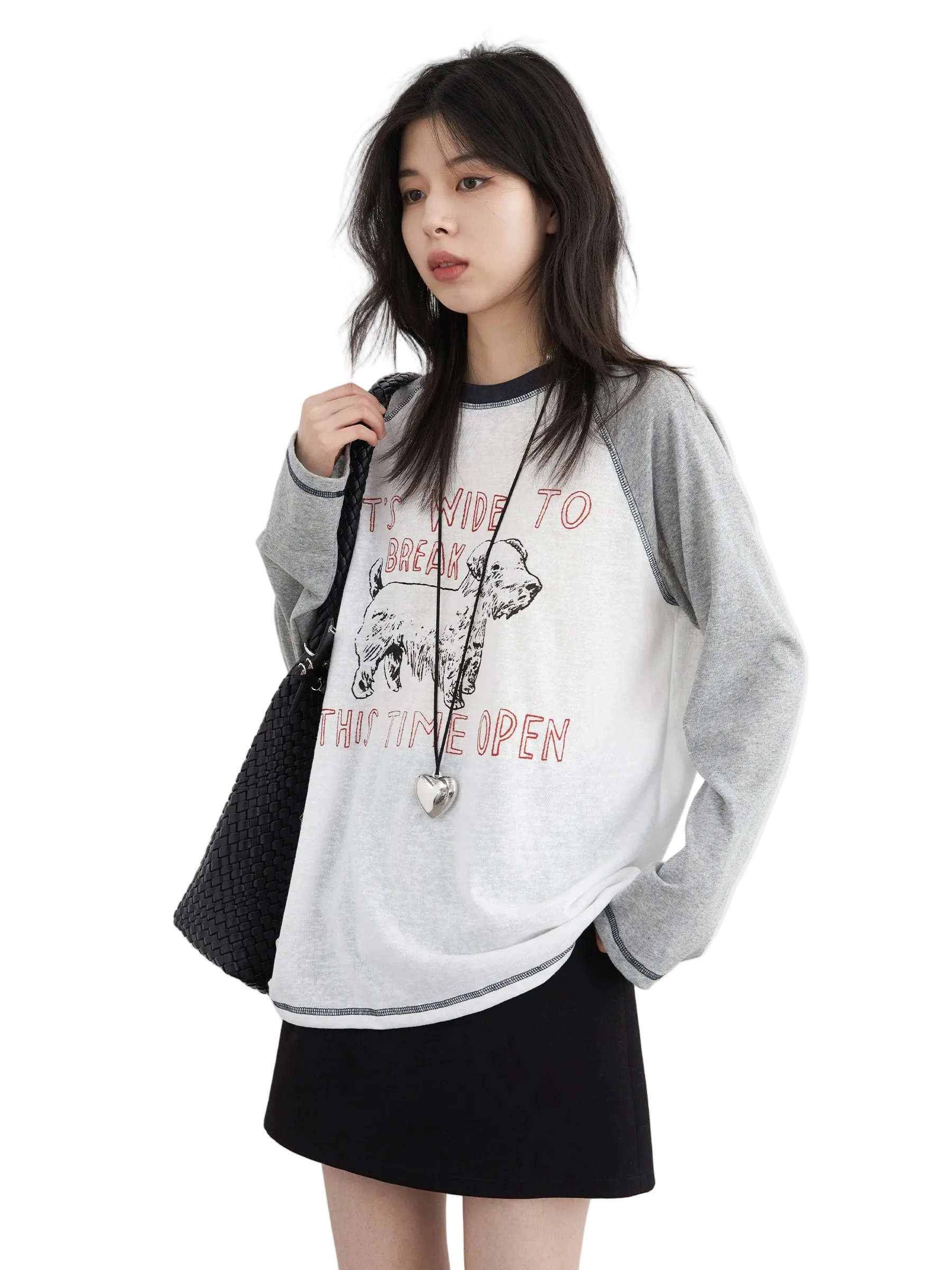 Woman wearing a gray oversized sweater with text and graphics, holding a black bag on a white background