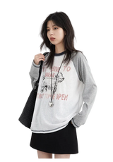 Woman wearing a gray and white sweatshirt with text and graphics, holding a black bag on a white background