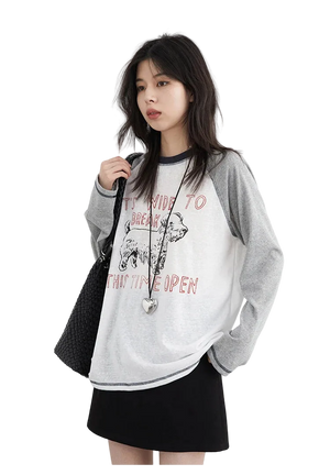 Woman wearing a gray and white sweatshirt with text and graphics, holding a black bag on a white background