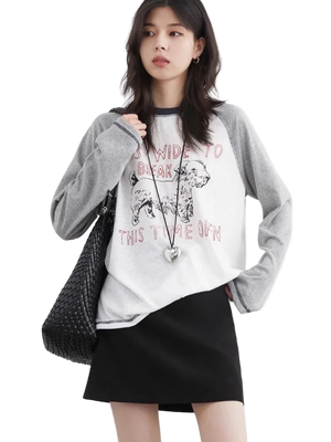 Woman wearing a white graphic t-shirt with a black skirt and gray cardigan on a light background