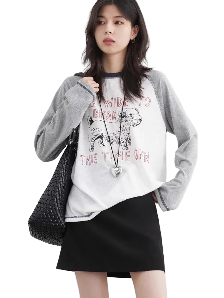 Woman wearing a white graphic t-shirt with a black skirt and gray cardigan on a light background