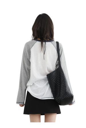 Person wearing a gray and white baseball-style shirt with a black woven bag on a white background