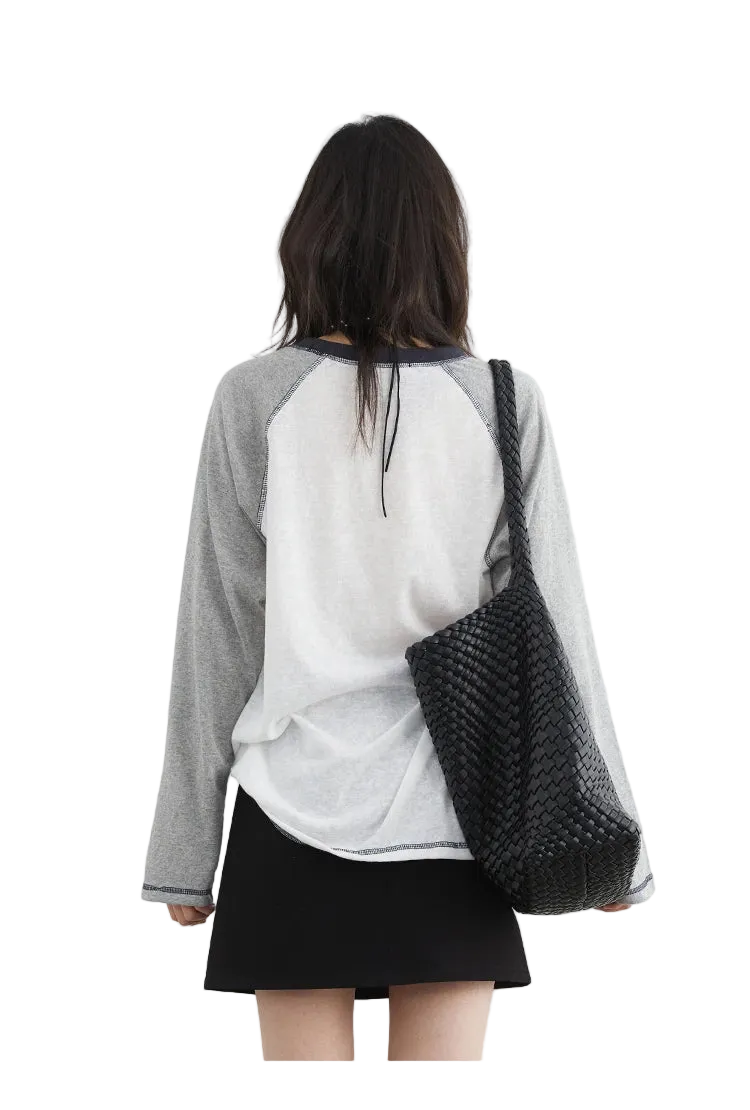Person wearing a gray and white baseball-style shirt with a black woven bag on a white background